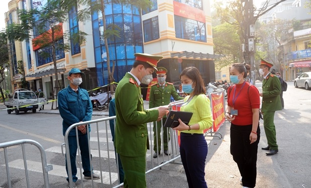 A police officer is checking access cards of on-duty people at the entrance gate of the quarantine zone.